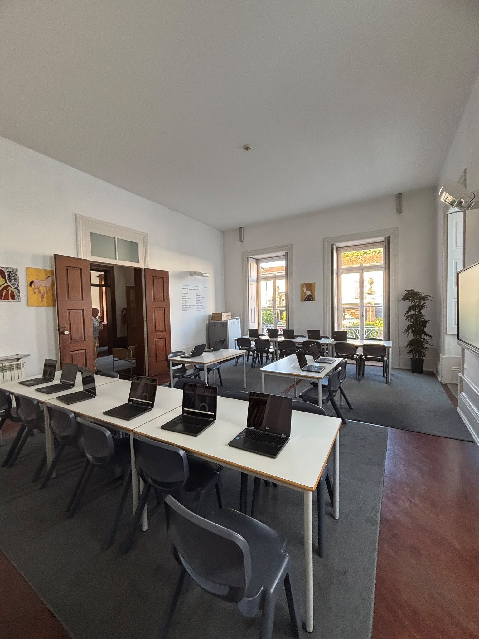 Biblioteca com mesas, computadores portáteis e janelas altas