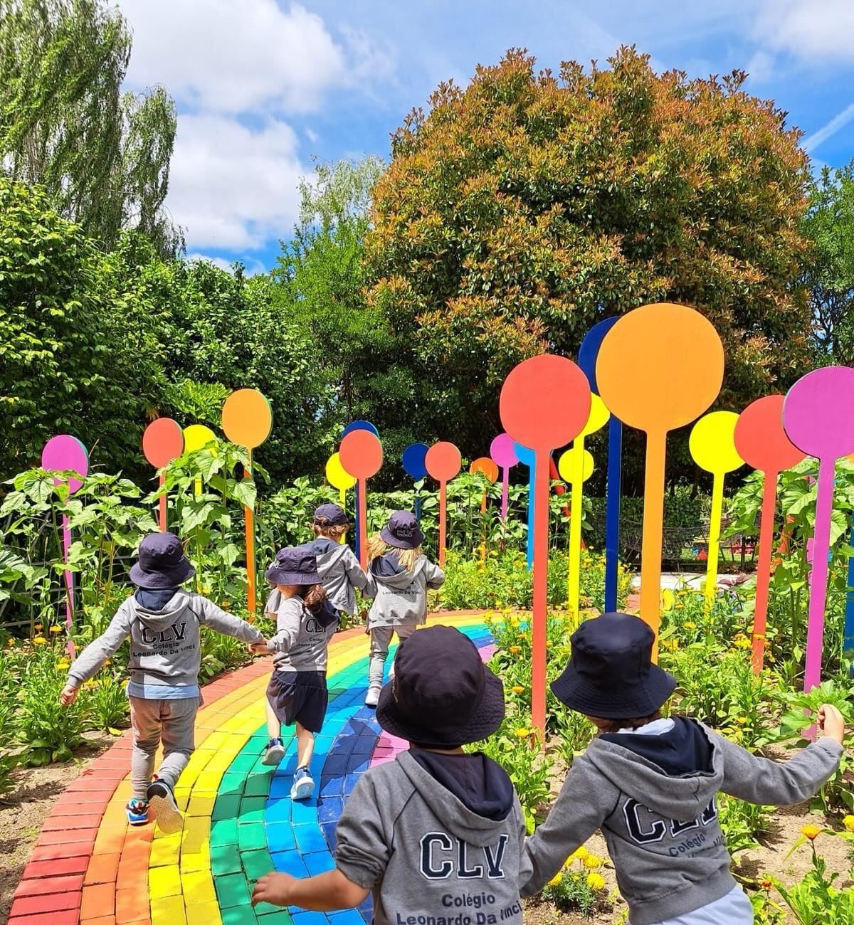 Crianças de costas a correr por um caminho pintado com as cores do arco-íris