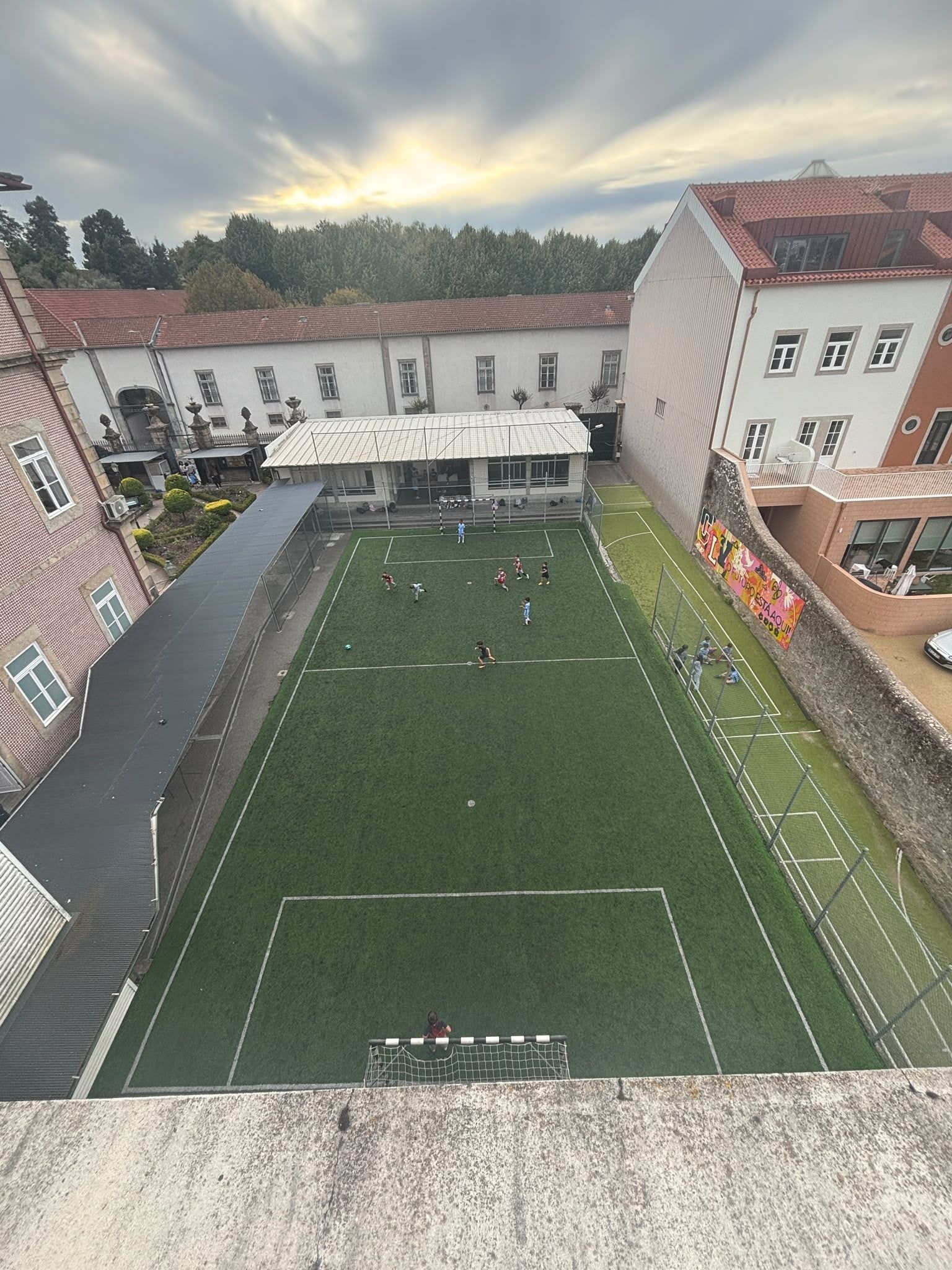 The sports pitch seen from above, with pupils playing and the school buildings around it, in the late afternoon
