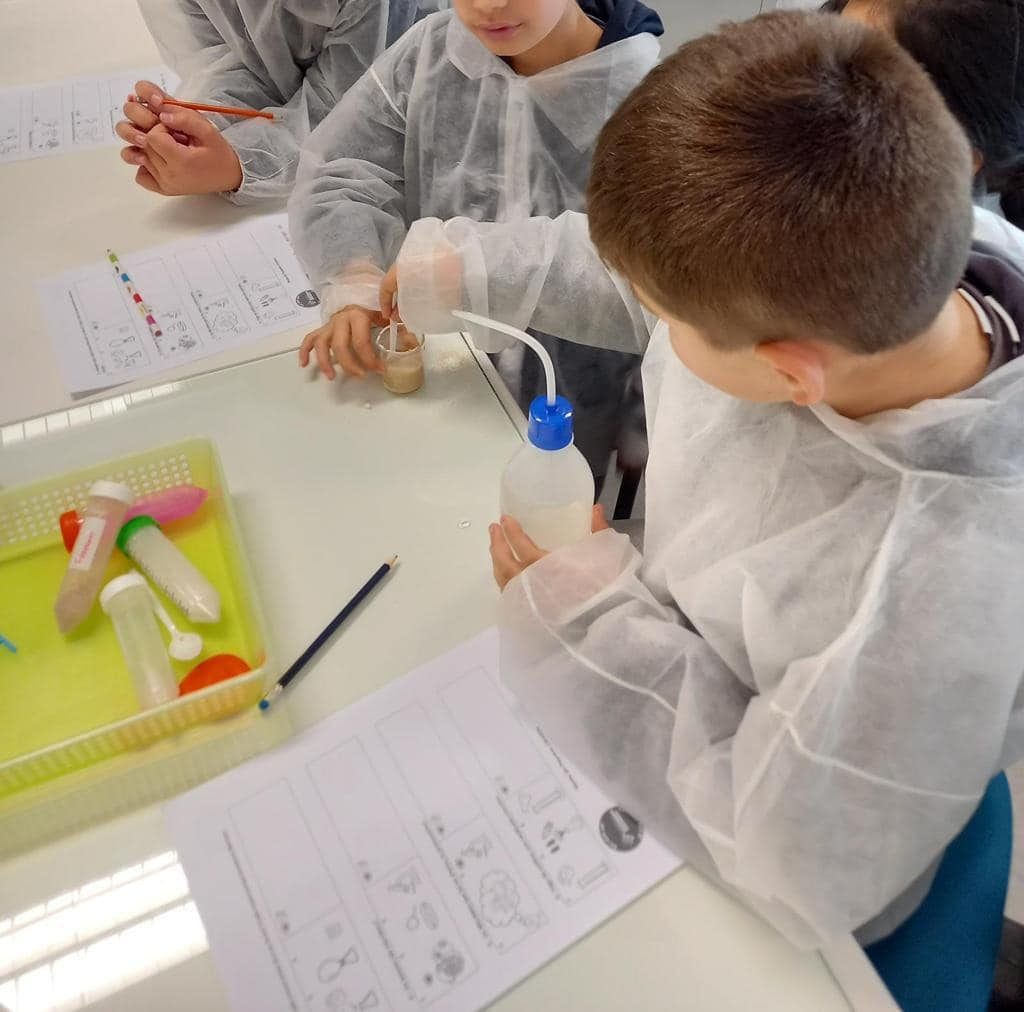 Pupils in white lab coats doing a science experiment with test tubes and worksheets