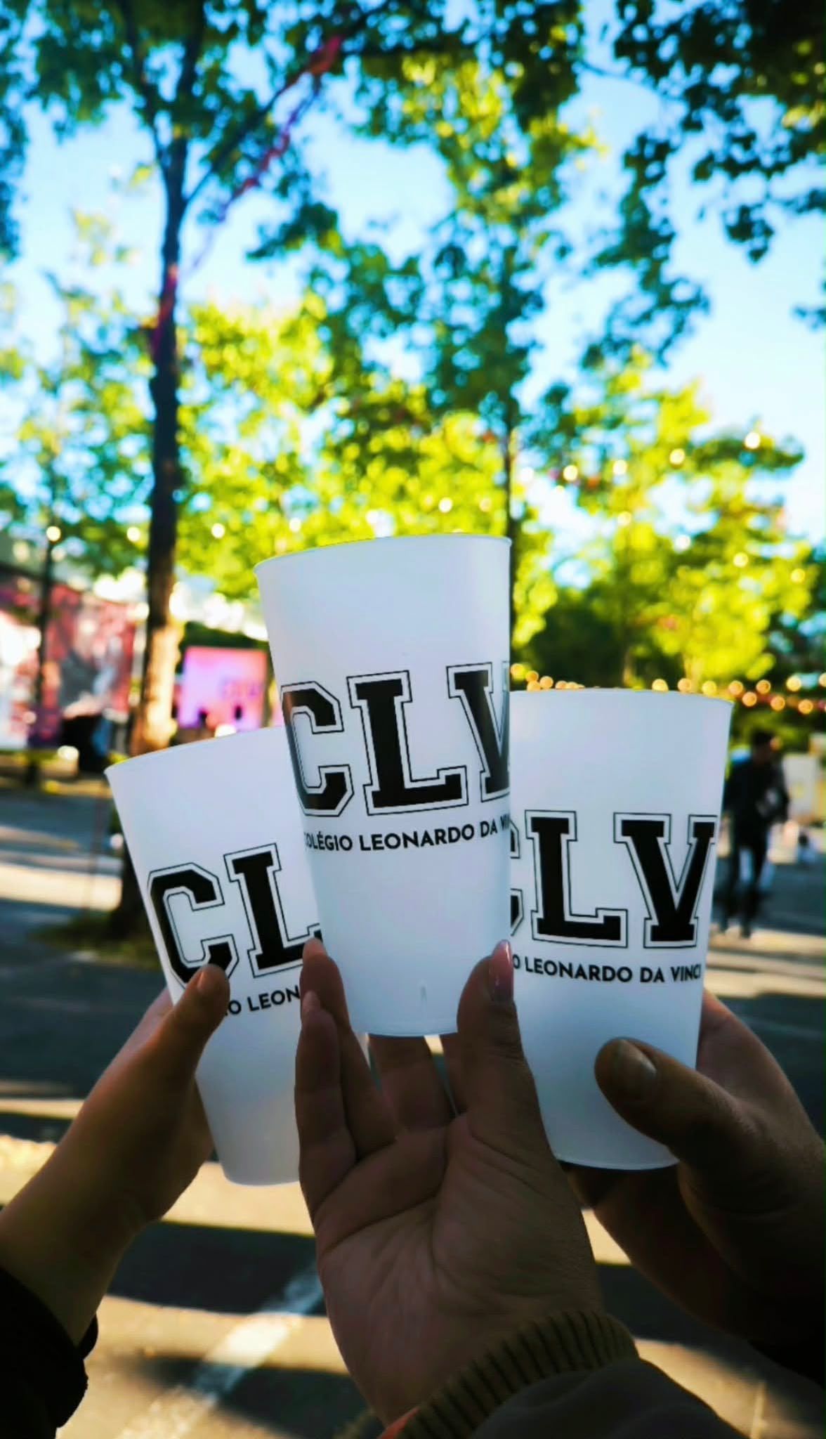 Três copos com o logótipo do colégio levantados num brinde, numa festa ao ar livre