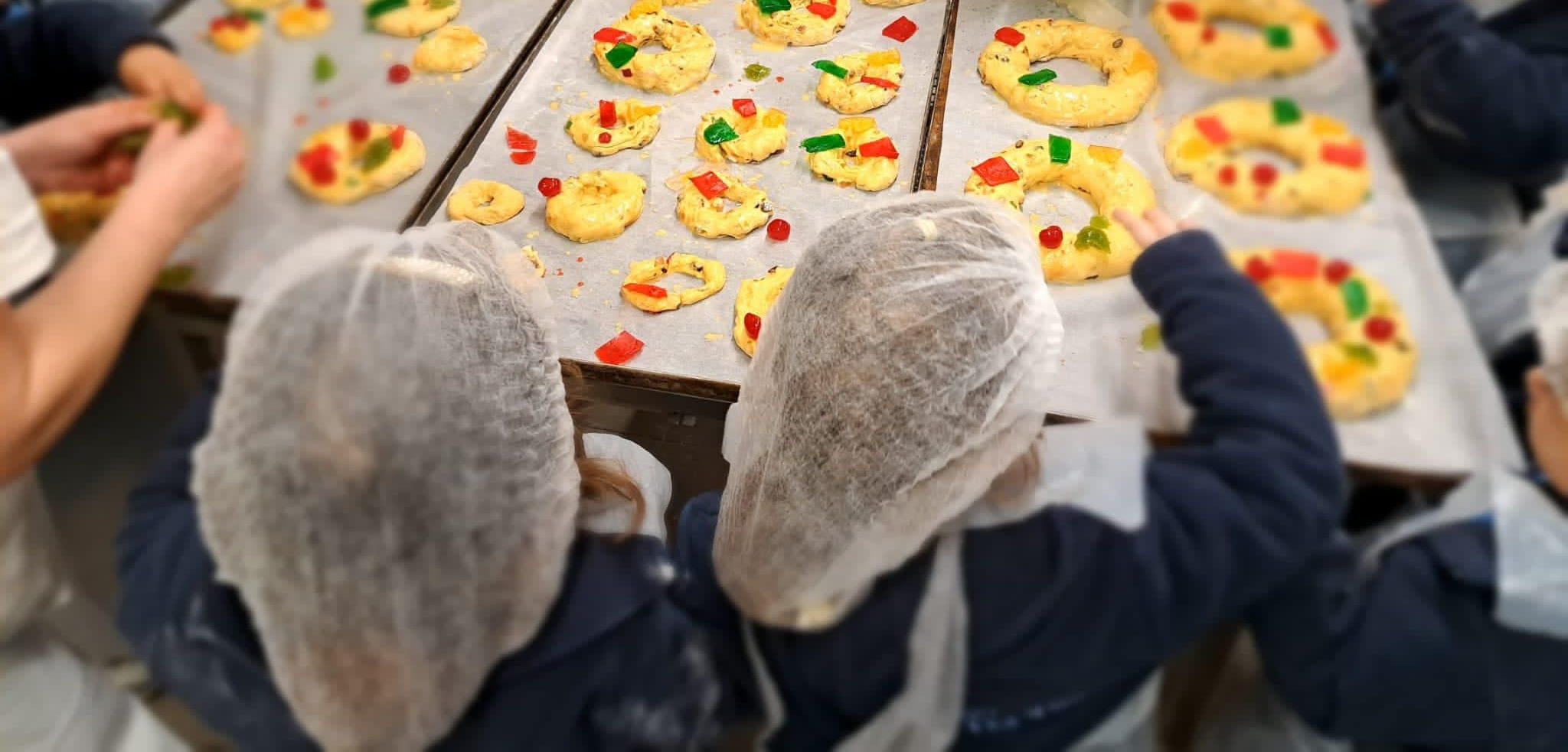 Alunos de touca e avental, vistos de costas, a decorar bolos-rei com fruta cristalizada