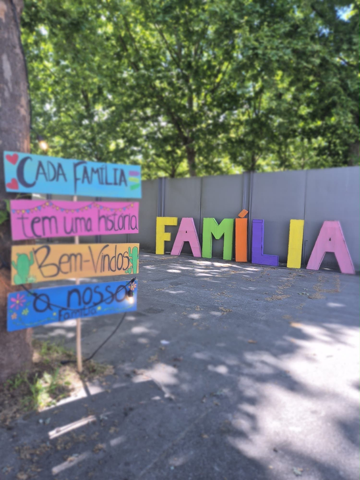 Hand-painted signs reading «Every family has a story, welcome to our family» and colourful letters spelling FAMÍLIA