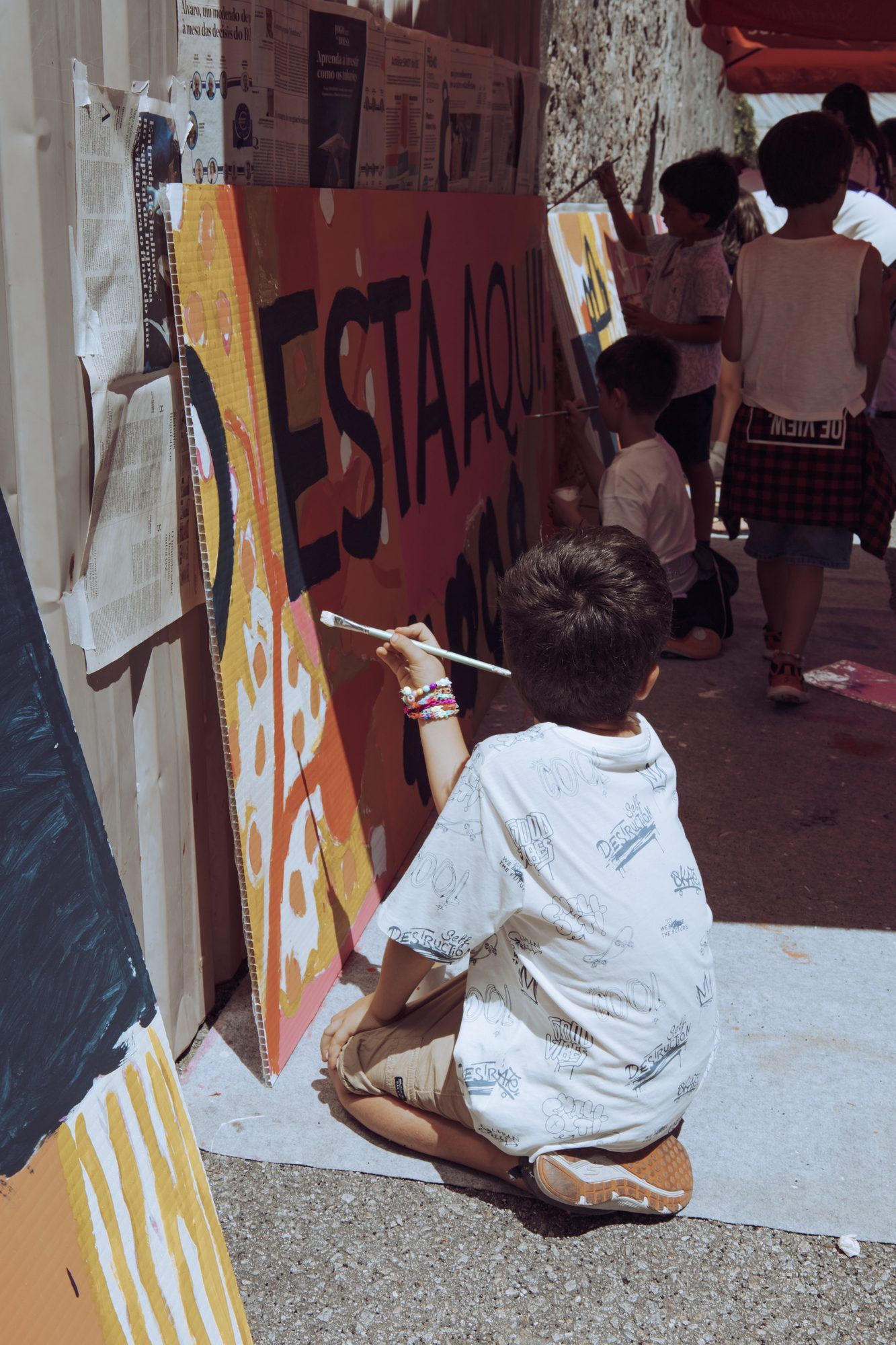 Aluno de joelhos a pintar um mural colorido, na festa de fim de ano