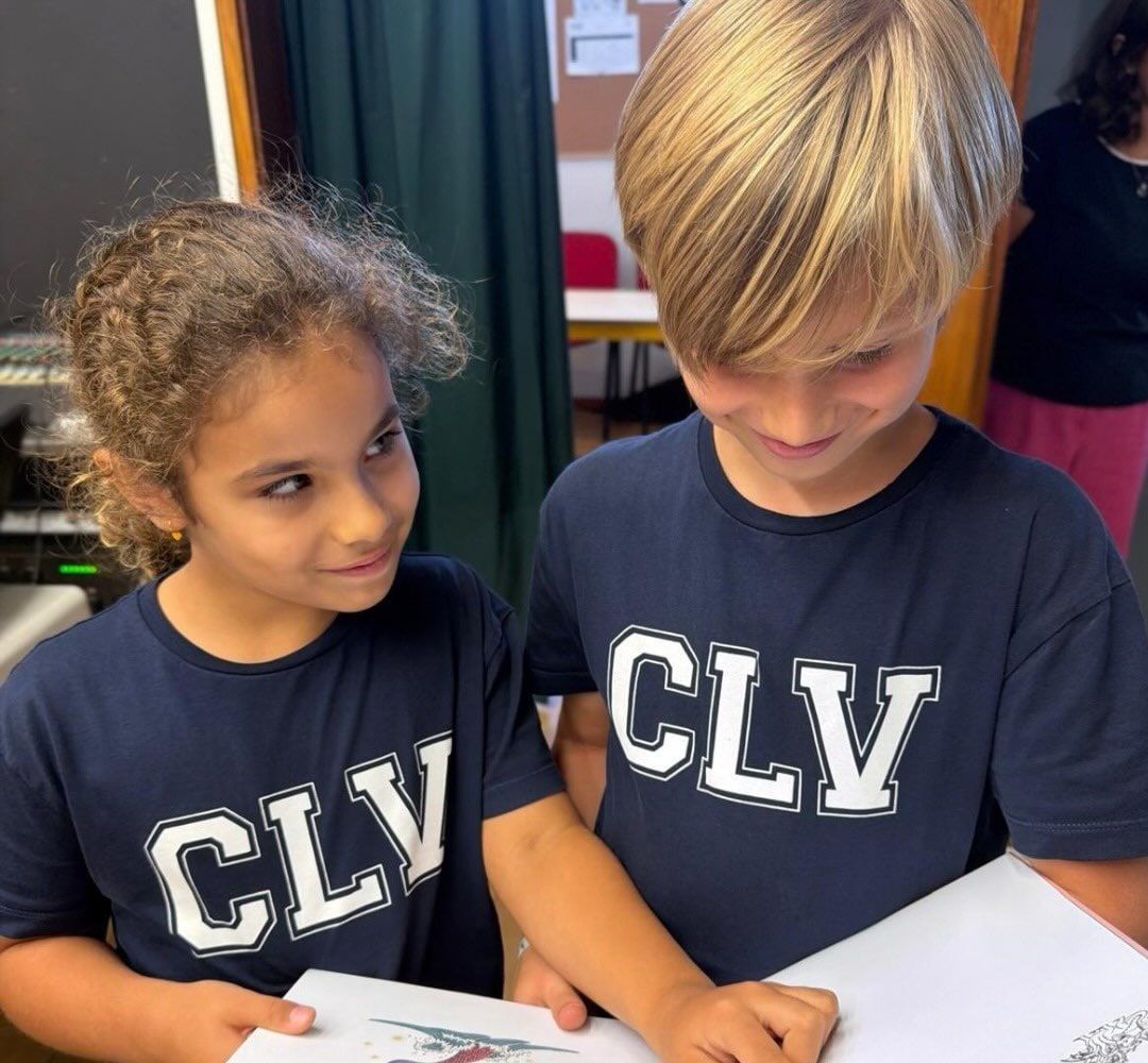 Dois alunos do 1.º Ciclo, com a t-shirt do colégio, a folhear um atlas