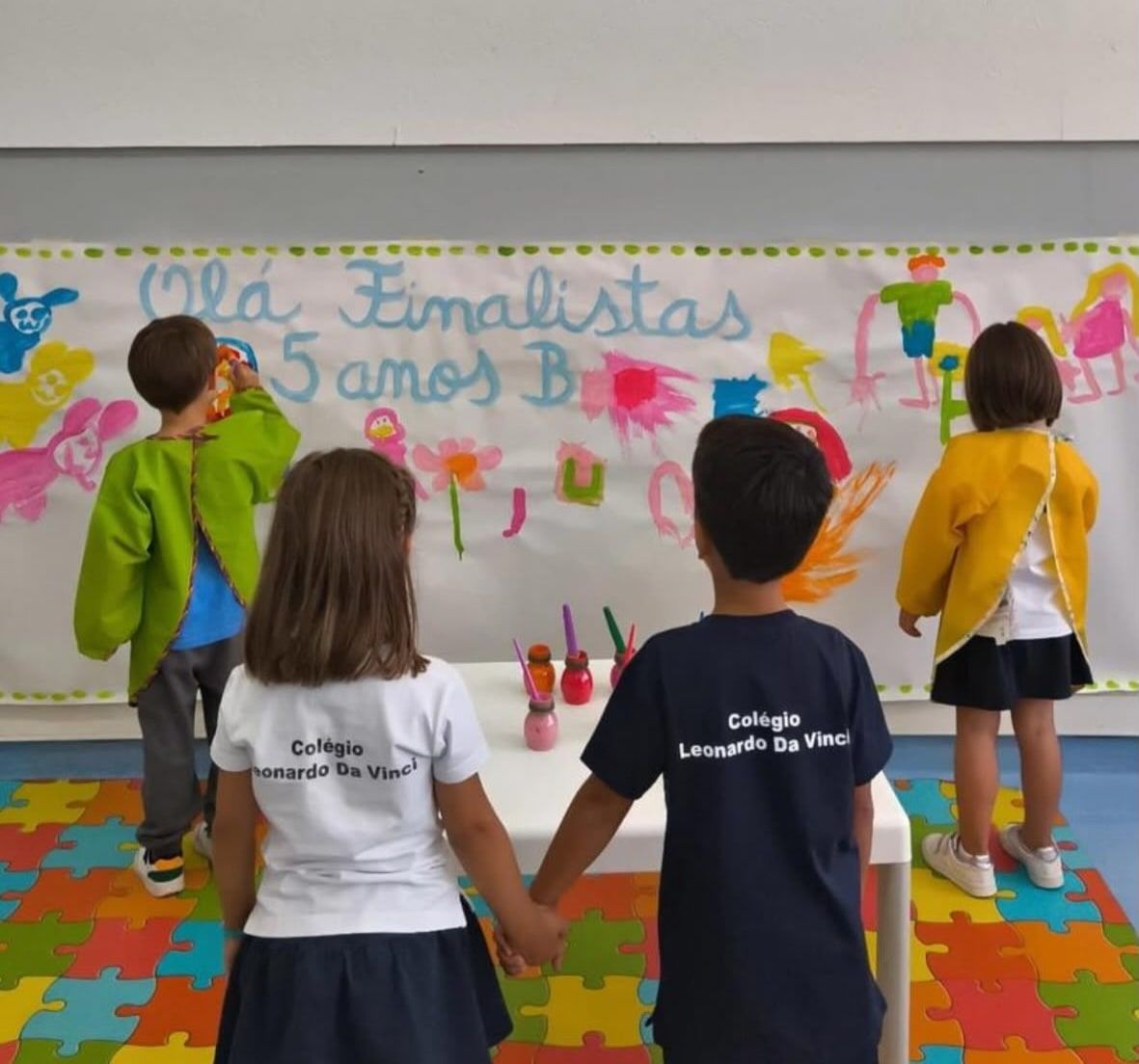 Crianças do Pré-escolar, de costas, a pintar um mural de boas-vindas aos finalistas