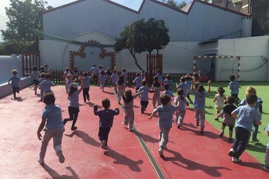 Crianças a correr e a brincar no recreio do colégio, num dia de sol