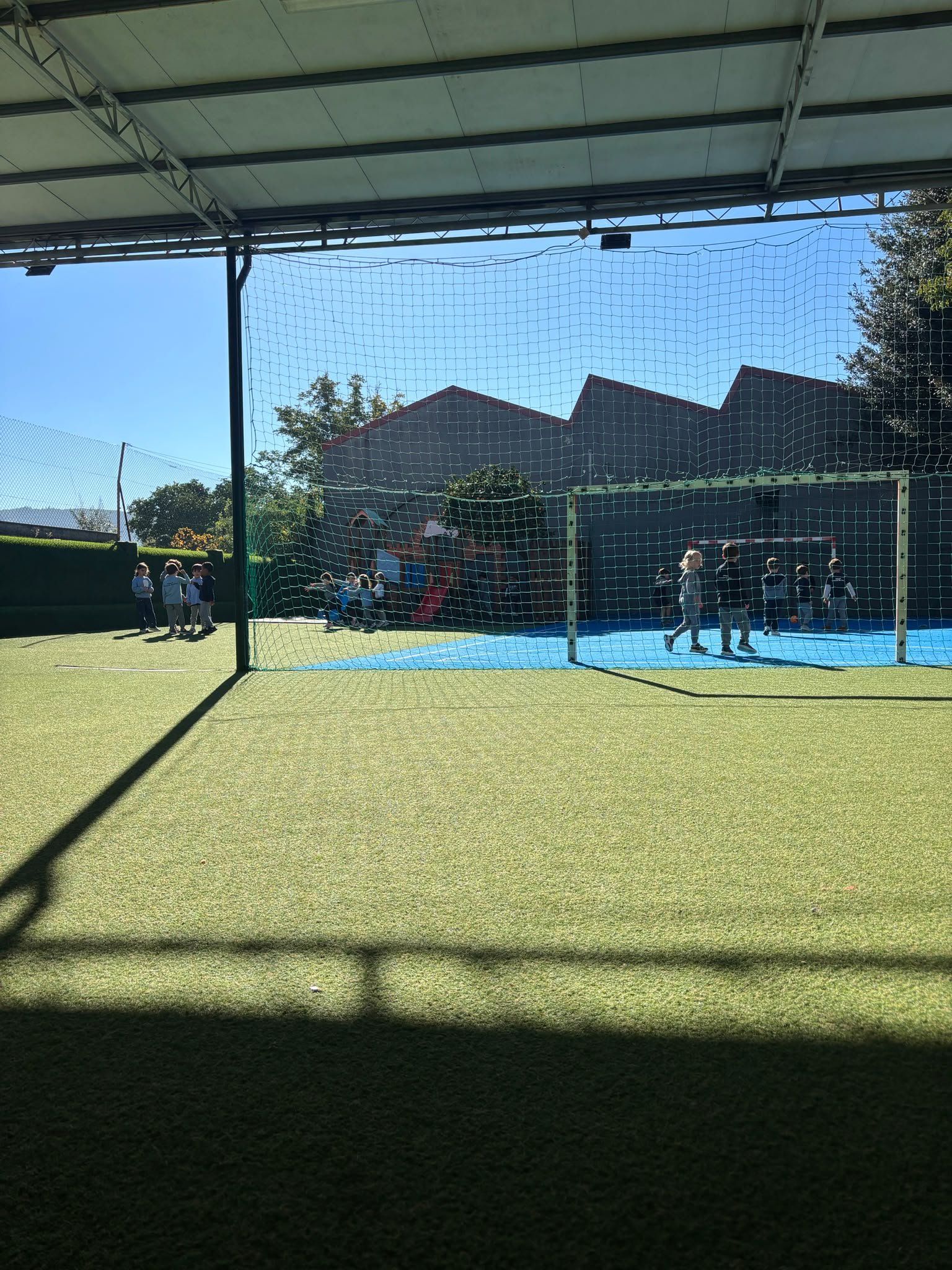 Recreio com relvado sintético, campo de jogos azul e escorrega, num dia de sol